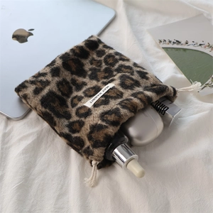 Detail of leopard print faux fur drawstring bag holding skincare bottles on white fabric