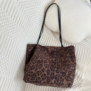 Detail of leopard print suede tote bag with black leather straps on soft white fabric