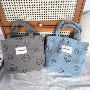 Detail of gray and blue corduroy tote bags featuring smiley patterns and logo patch