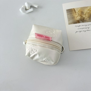 Close-up of cream PU leather earphone case with embossed bow pattern and pearl charm