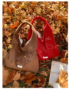 Detail of bird embroidery on velvet tote bag among autumn leaves and vintage book