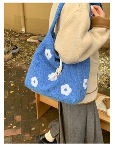 Close-up of blue plush shoulder bag with white flower embroidery and faux shearling texture