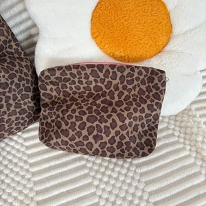 Detail of leopard print suede pouch with purple zipper on a decorative pillow