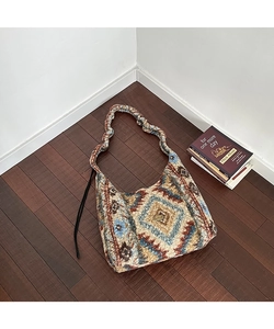 Dettaglio borsa boho in maglia con motivo etnico a rombi e targhetta in metallo fatta a mano