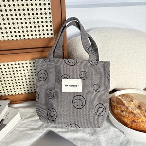 Detail of grey corduroy handbag with black smiley face prints and woven label