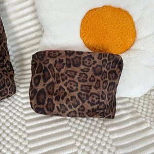 Detail of leopard print suede pouch with pink zipper on soft textured background