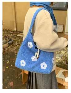 Close-up of blue plush shoulder bag with white flower embroidery and drawstring detail