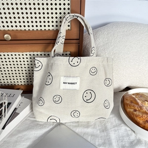 Detailed texture of white corduroy tote bag featuring minimalist black smiley face patterns