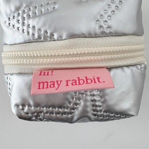 Detail view of silver PU earphone pouch with wavy quilting and hi! may rabbit label