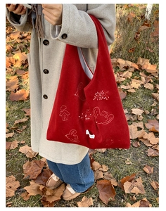 Close-up of red velvet tote bag with white bird embroidery in autumn outdoor setting