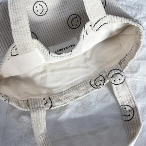 Close-up of beige corduroy tote with smiley face print and May Rabbit woven inner label