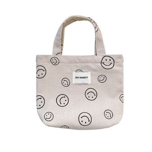 Beige corduroy handbag with smiley face print and woven brand label on white background