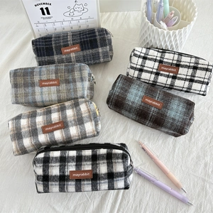 Flat lay of multiple wool plaid pencil cases with leather labels on soft white fabric