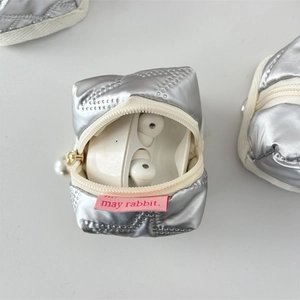 Macro detail of quilted silver PU earphone case with pearl charm and smooth zipper