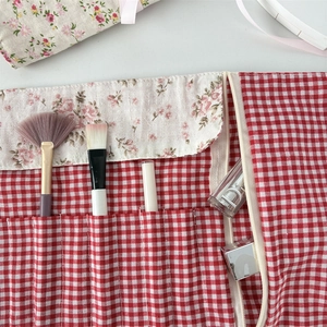 Detail view of red gingham makeup brush roll with floral fabric lining and zipper compartment