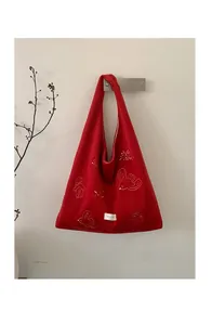 Detailed view of red tote bag with intricate bird embroidery and brand label on fabric