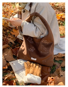 Close-up of bird embroidery on brown tote bag with warm winter gloves on autumn leaves