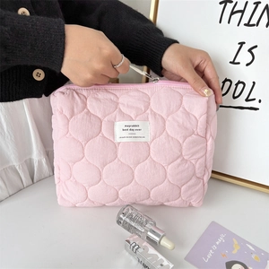 Close-up of pink quilted cosmetic bag with soft texture and brand label on white desk