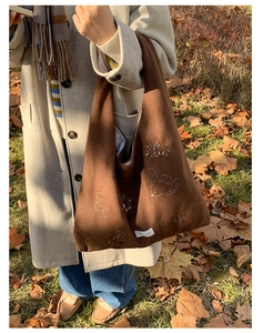 Detailed embroidery of birds and houses on a dark brown suede tote bag in autumn light