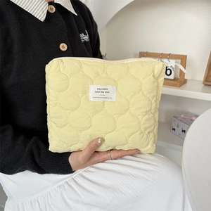 Detail of light yellow quilted makeup bag with zipper closure and soft cotton texture