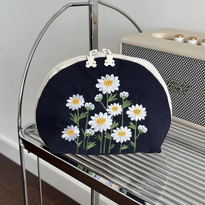 Dettaglio della pochette blu scuro con ricamo a margherita e zip a forma di orso
