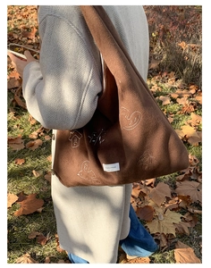 Close-up of bird embroidery detail on brown velvet tote bag with branded woven label