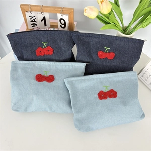 Détail macro de la trousse de maquillage en denim avec broderie cerise et zip en métal