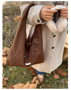 Close-up detail of bird embroidery on a brown canvas tote bag for autumn commuting