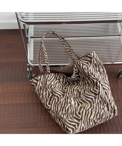 Detail of zebra print plush tote bag with gold Handmade metal plaque in indoor setting
