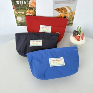 Three compact nylon makeup bags in red, black and blue shown on a stylish lifestyle desk