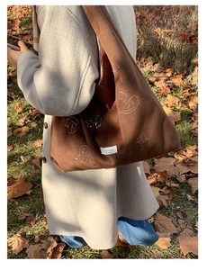 Close-up of bird embroidery and branded label on dark brown felt tote shoulder bag