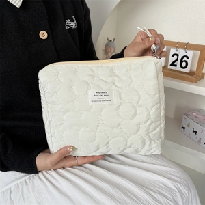 White floral quilted cosmetic bag with ribbon zipper held by model in warm setting