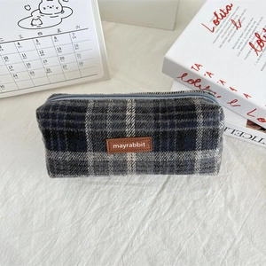 Close-up of a grey plaid wool pencil case with a brown leather tag on a desk
