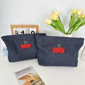 Détail des trousses de toilette en denim bleu avec broderie cerise en relief 3D