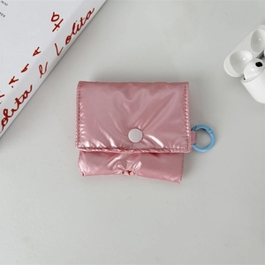 Pink quilted puffer AirPods case with snap closure and blue metal carabiner on white desk