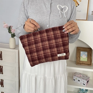 Brown and beige plaid canvas clutch bag held by hand in a minimalist home setting