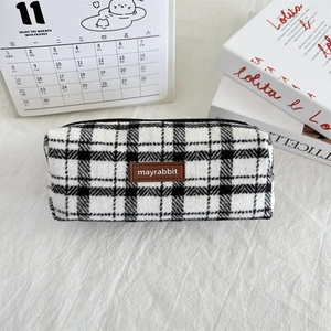 Close-up of checkered tweed pencil case with brown leather tag on minimalist desk