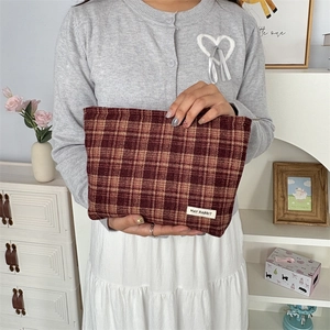 Detail of red-brown checkered canvas pouch held by hands showing premium fabric texture