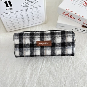 Detail of checkered wool pencil case with zipper and brown leather brand patch