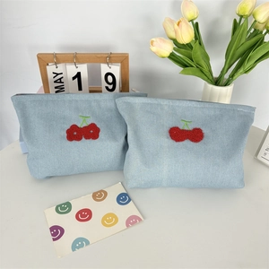 Détail de trousses à maquillage en denim bleu clair avec broderie cerise rouge
