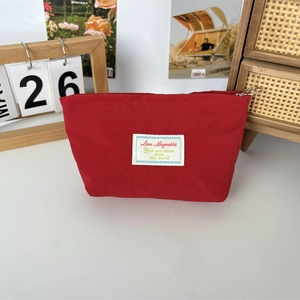 Close-up of a small red fabric makeup bag with top zipper and stylish label detail