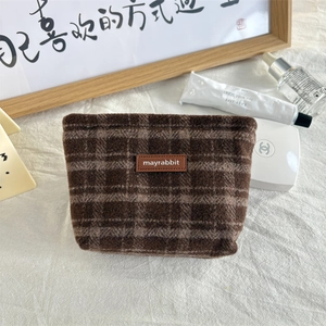 Detail van een bruin geruite cosmetische tas met leren label op wit linnen oppervlak