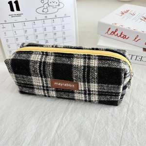 Detail of checkered plaid fabric pencil case with yellow zipper and brown leather logo tag