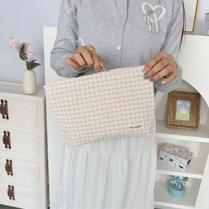 Roze en wit geruite canvas make-uptas met rits vastgehouden door model in huiselijke sfeer