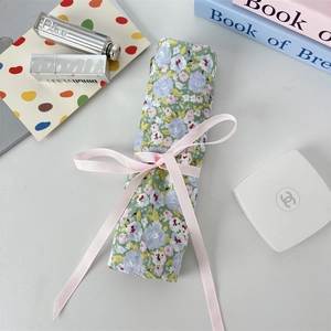 Detail of floral fabric makeup brush roll with pink ribbon bow and elegant accessories