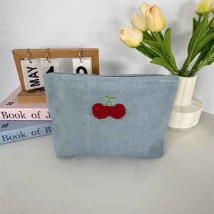 Détail de la trousse à maquillage en jean bleu clair avec broderie cerise rouge en 3D