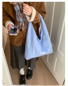 Detail of light blue knitted tote bag with bird embroidery on model in casual setting
