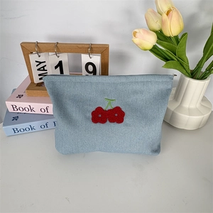 Détail de la broderie cerise rouge sur une trousse de maquillage en tissu bleu