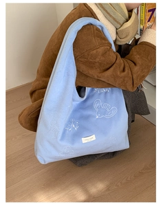Detail of light blue fuzzy tote bag with intricate bird and floral white embroidery