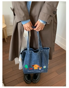 Detail of embroidered cartoon puppy and nature motifs on a blue denim tote bag
